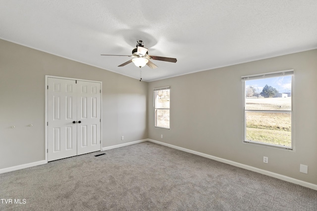 unfurnished bedroom featuring lofted ceiling, a textured ceiling, a closet, carpet, and baseboards