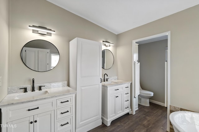 bathroom featuring wood finished floors, two vanities, baseboards, and a sink