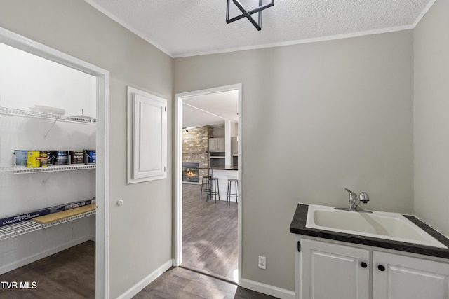 laundry room with dark wood-type flooring, baseboards, ornamental molding, a textured ceiling, and a sink