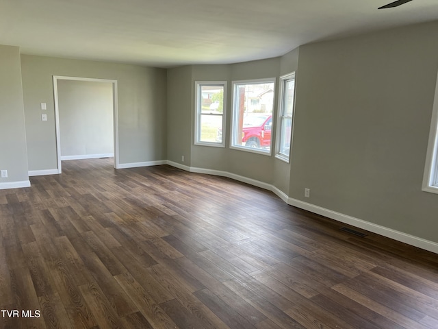 empty room featuring visible vents, baseboards, and dark wood finished floors