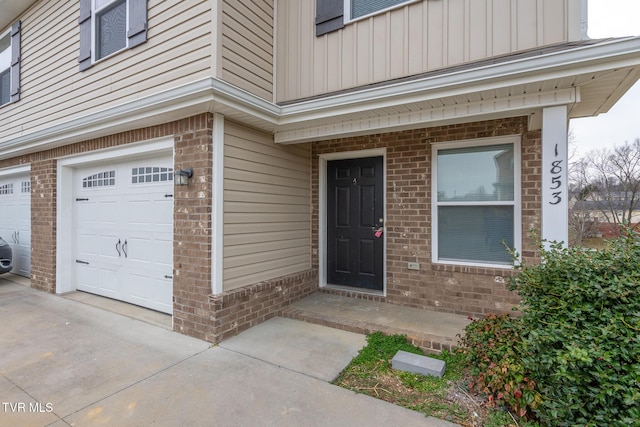 property entrance featuring board and batten siding, concrete driveway, brick siding, and a garage