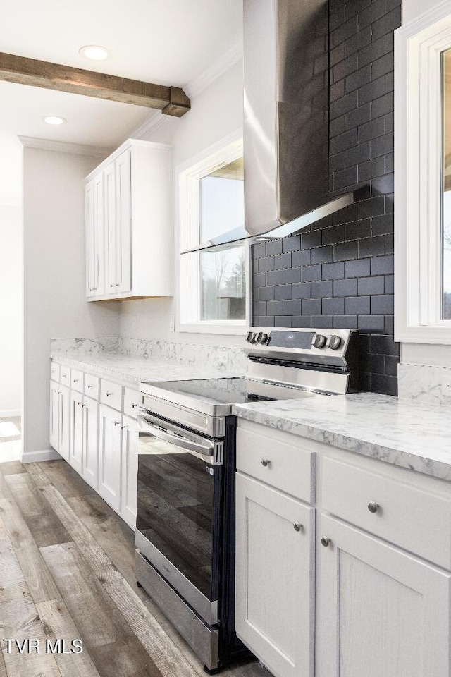 kitchen with light wood-style flooring, stainless steel electric stove, wall chimney exhaust hood, white cabinets, and decorative backsplash