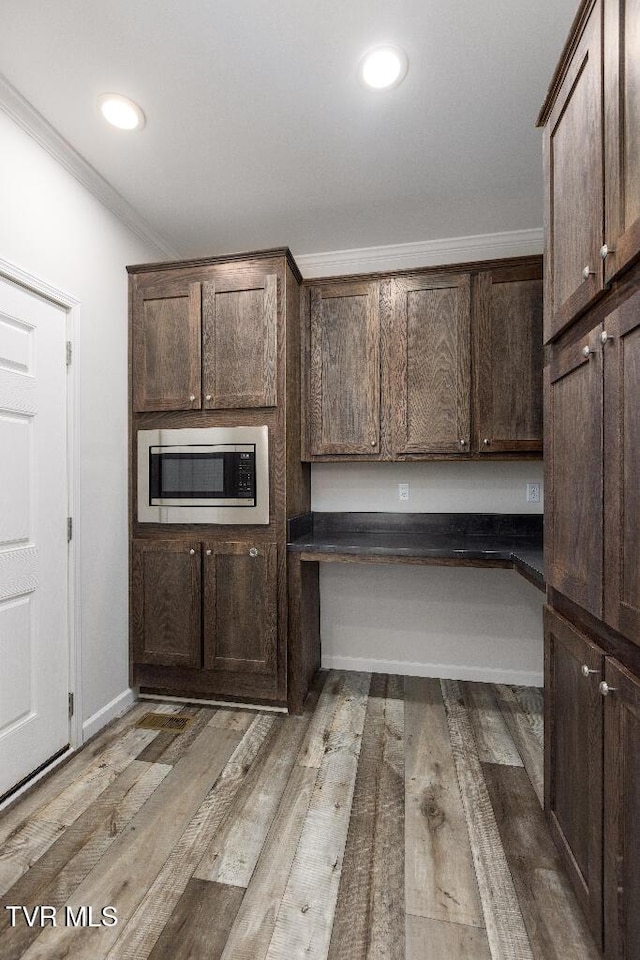 kitchen with dark countertops, stainless steel microwave, light wood finished floors, crown molding, and dark brown cabinetry