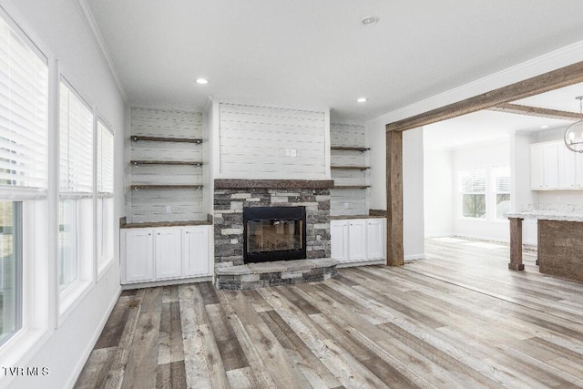 unfurnished living room with baseboards, light wood-style flooring, recessed lighting, a stone fireplace, and crown molding