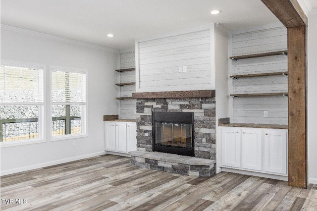 unfurnished living room with light wood-style flooring, a fireplace, crown molding, and baseboards