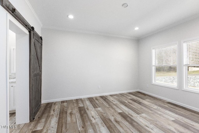 interior space with multiple windows, light wood-style flooring, a barn door, and ornamental molding