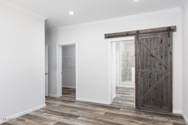 spare room with a barn door, ornamental molding, baseboards, and wood finished floors