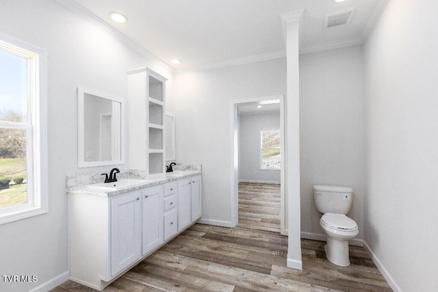 full bathroom featuring visible vents, crown molding, double vanity, wood finished floors, and a sink