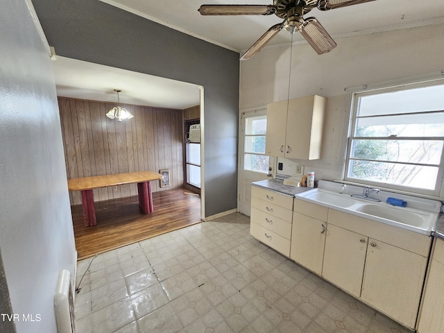 kitchen featuring a sink, wood walls, light countertops, light floors, and ceiling fan