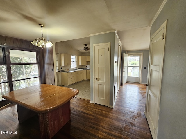 dining room featuring ornamental molding, ceiling fan with notable chandelier, dark wood finished floors, wooden walls, and baseboards