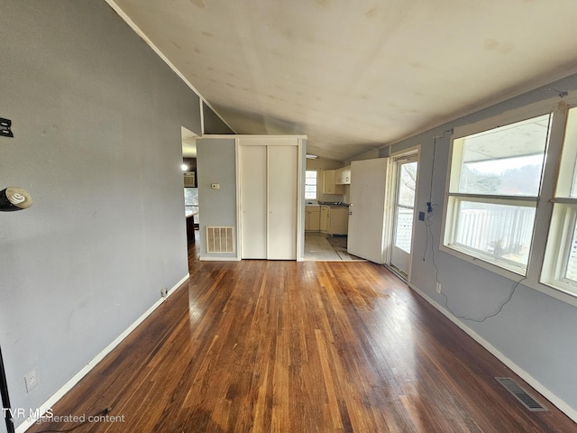 unfurnished living room with lofted ceiling, wood finished floors, visible vents, and baseboards