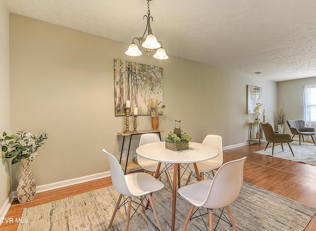 dining area featuring a textured ceiling, baseboards, an inviting chandelier, and wood finished floors
