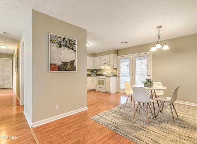 dining space with a textured ceiling, light wood-type flooring, and baseboards