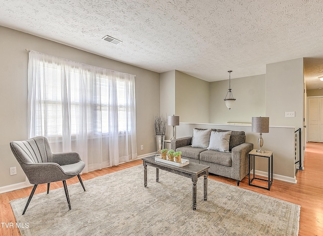 living area with baseboards, visible vents, light wood finished floors, and a textured ceiling