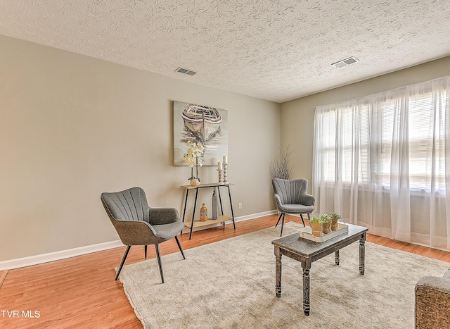 living area with visible vents, baseboards, a textured ceiling, and light wood-style flooring