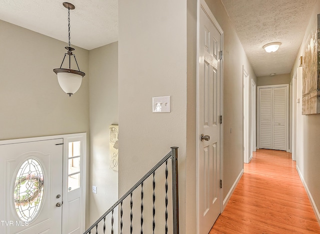 foyer with light wood-style flooring, baseboards, and a textured ceiling
