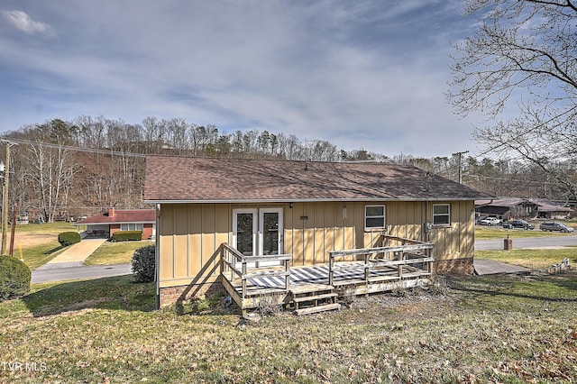 rear view of house with a wooden deck, a shingled roof, and a yard