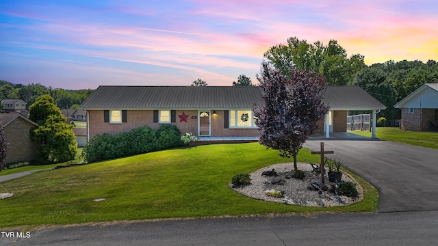 ranch-style home with an attached carport, a yard, aphalt driveway, brick siding, and metal roof