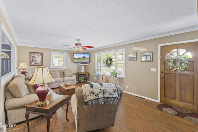 living room with a ceiling fan, wood finished floors, baseboards, visible vents, and crown molding