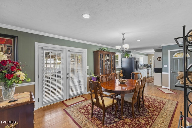 dining area with light wood-style flooring, plenty of natural light, a chandelier, and crown molding