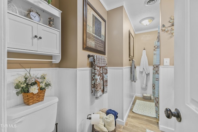 bathroom featuring visible vents, a wainscoted wall, toilet, ornamental molding, and wood finished floors