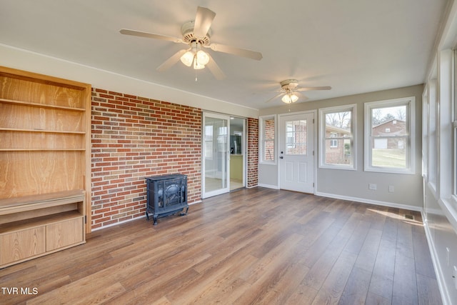 unfurnished living room featuring baseboards, a wood stove, ceiling fan, and wood finished floors