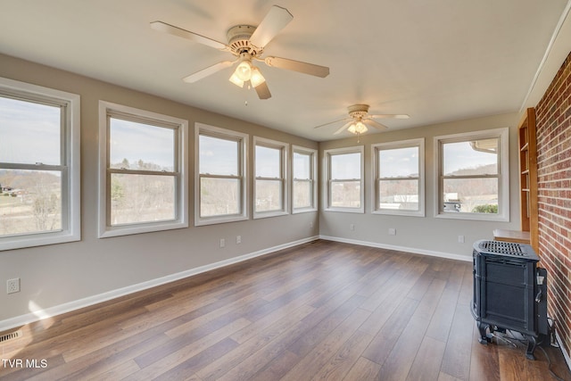 unfurnished sunroom with visible vents, a wood stove, and a ceiling fan