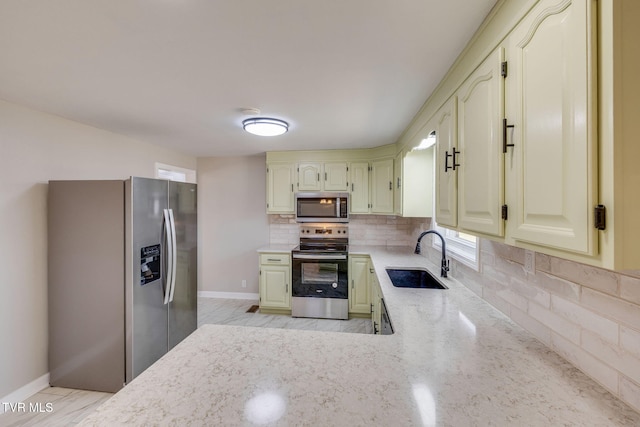 kitchen featuring a sink, backsplash, stainless steel appliances, baseboards, and light stone countertops