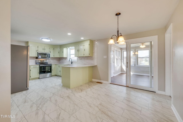 kitchen with a peninsula, a sink, light countertops, appliances with stainless steel finishes, and tasteful backsplash