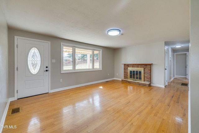 foyer entrance with a brick fireplace, light wood-style floors, visible vents, and baseboards