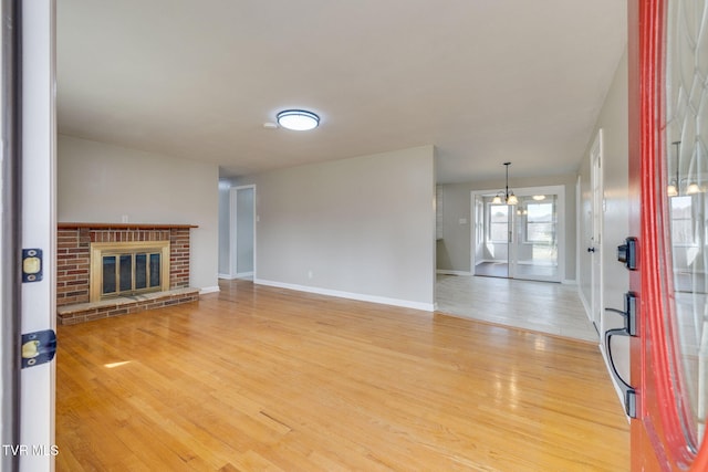 unfurnished living room featuring baseboards, a brick fireplace, and wood finished floors