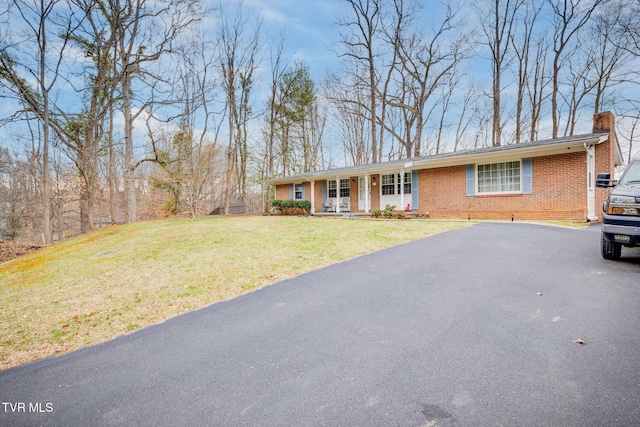 ranch-style home with a front yard, driveway, a porch, a chimney, and brick siding
