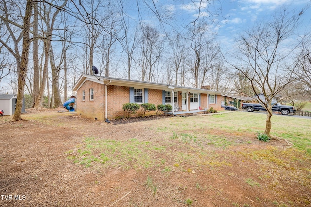 view of front of property with brick siding, a porch, an outdoor structure, and a front lawn