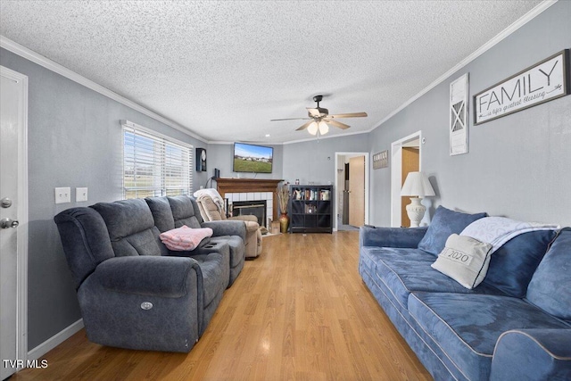 living room featuring crown molding, ceiling fan, light wood-style flooring, a fireplace, and a textured ceiling