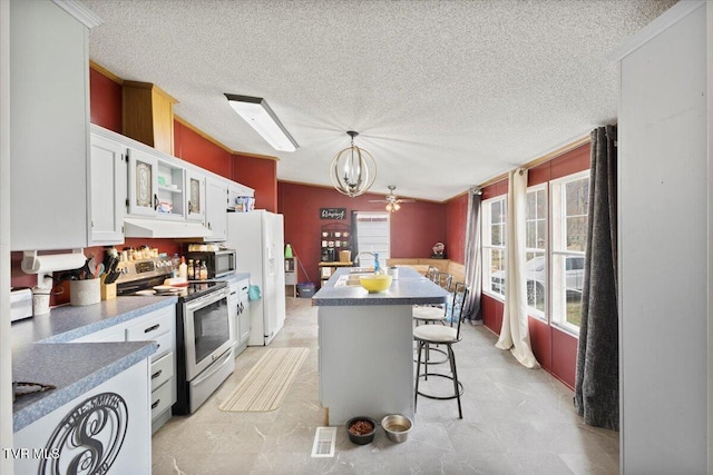 kitchen with a sink, glass insert cabinets, appliances with stainless steel finishes, white cabinetry, and a chandelier