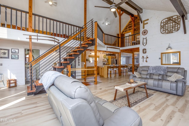living area featuring beam ceiling, stairs, a ceiling fan, and wood finished floors