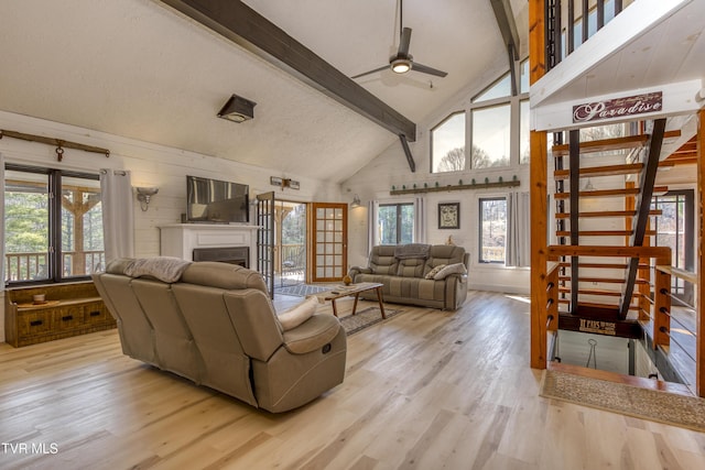 living room with light wood-type flooring, beamed ceiling, high vaulted ceiling, a ceiling fan, and a fireplace