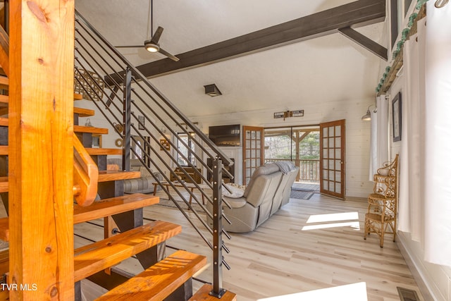 stairs featuring wooden walls, a ceiling fan, wood finished floors, visible vents, and vaulted ceiling with beams