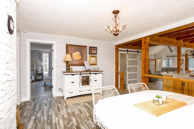 dining area with lofted ceiling, a barn door, wood finished floors, a notable chandelier, and a textured ceiling