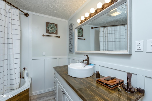 bathroom featuring vanity, wood finished floors, a wainscoted wall, a textured ceiling, and a decorative wall
