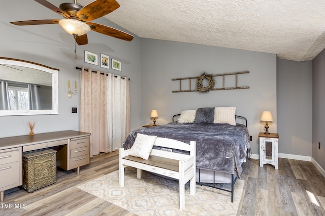 bedroom featuring baseboards, light wood-type flooring, lofted ceiling, a textured ceiling, and a ceiling fan