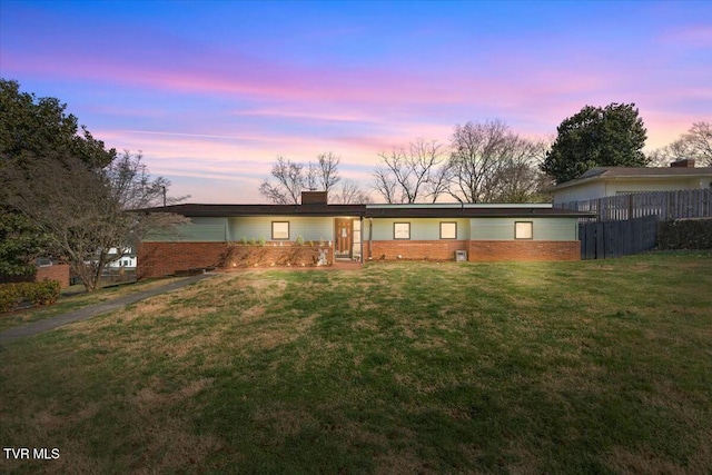 view of front of home with fence, a lawn, brick siding, and a chimney