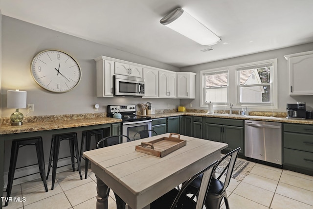 kitchen with light tile patterned floors, white cabinets, appliances with stainless steel finishes, and a sink