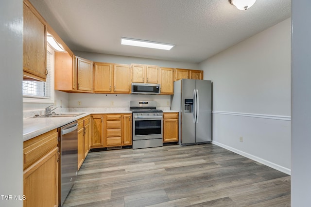 kitchen with light wood finished floors, a sink, stainless steel appliances, light countertops, and a textured ceiling