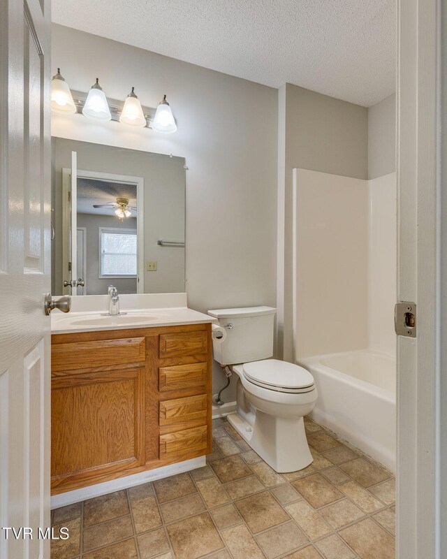full bathroom featuring toilet, vanity,  shower combination, a textured ceiling, and a ceiling fan