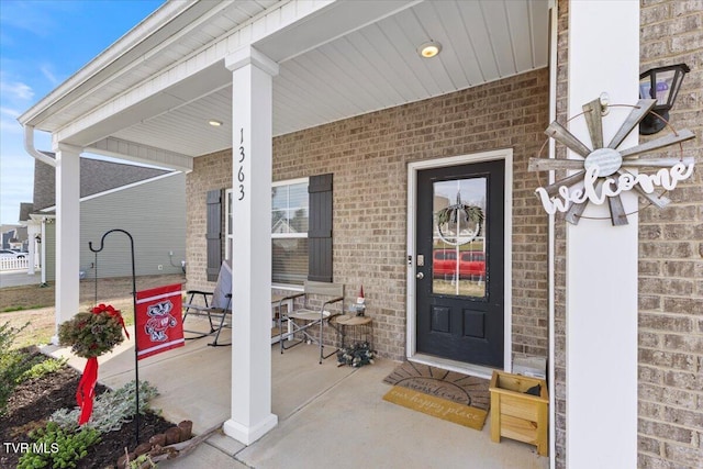view of exterior entry with brick siding and covered porch