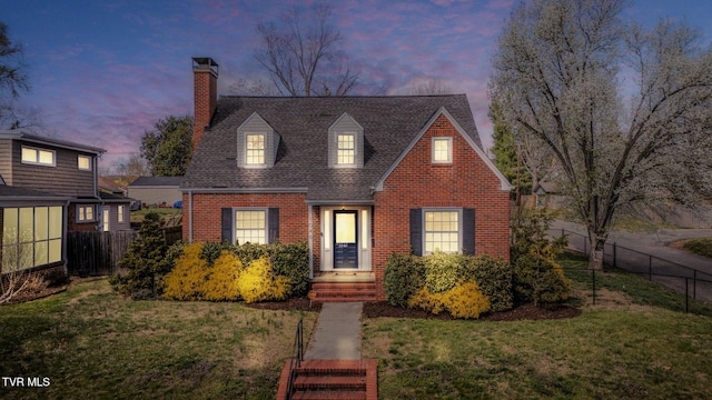 new england style home with brick siding, fence, a chimney, and a front yard