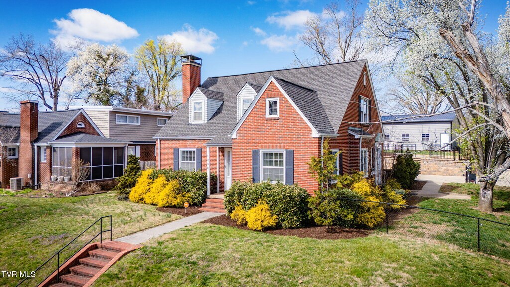 view of front facade featuring a sunroom, fence, a front yard, brick siding, and a chimney