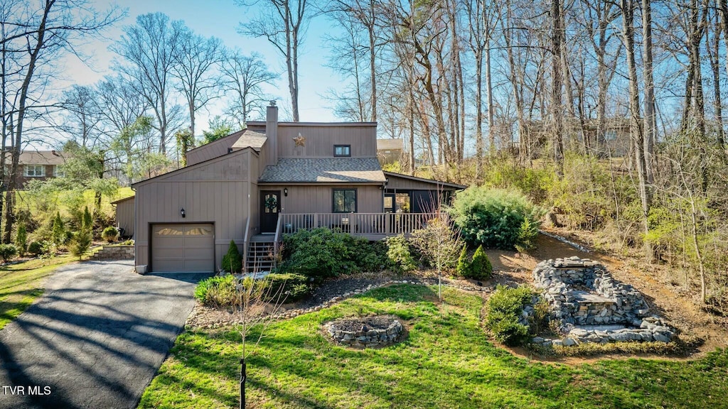 view of front facade featuring driveway, an outdoor fire pit, an attached garage, a shingled roof, and a chimney