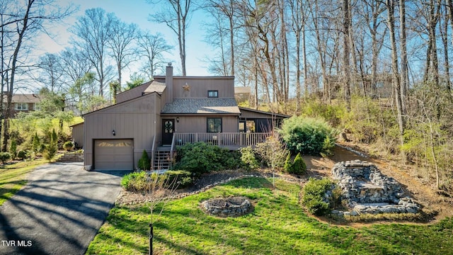 view of front facade featuring driveway, an outdoor fire pit, an attached garage, a shingled roof, and a chimney